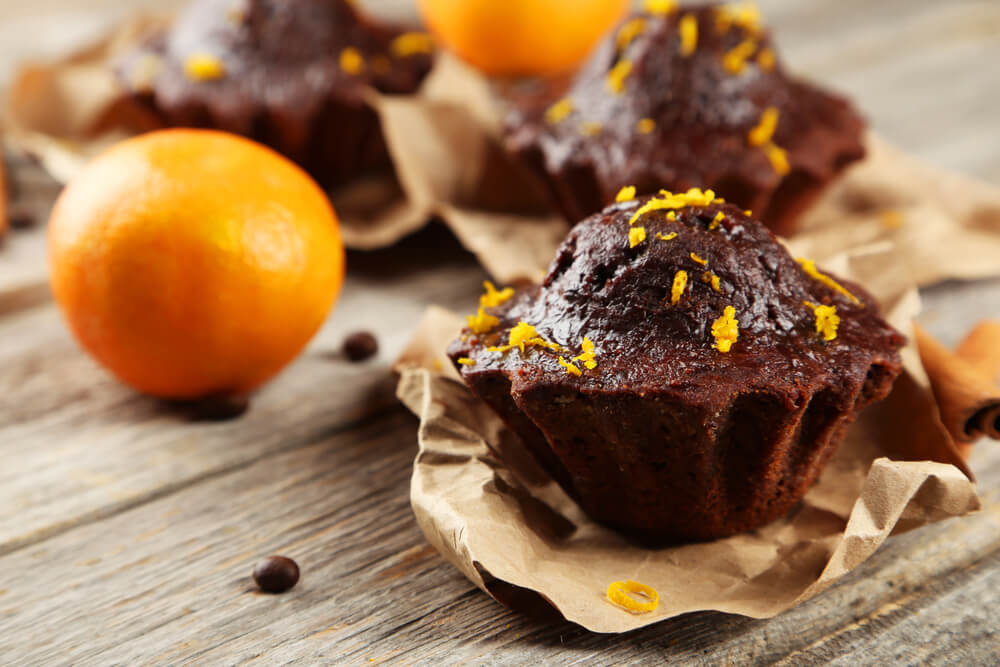 Čokoládové muffiny s pomarančovou kôrou a celým pomarančom v pozadí